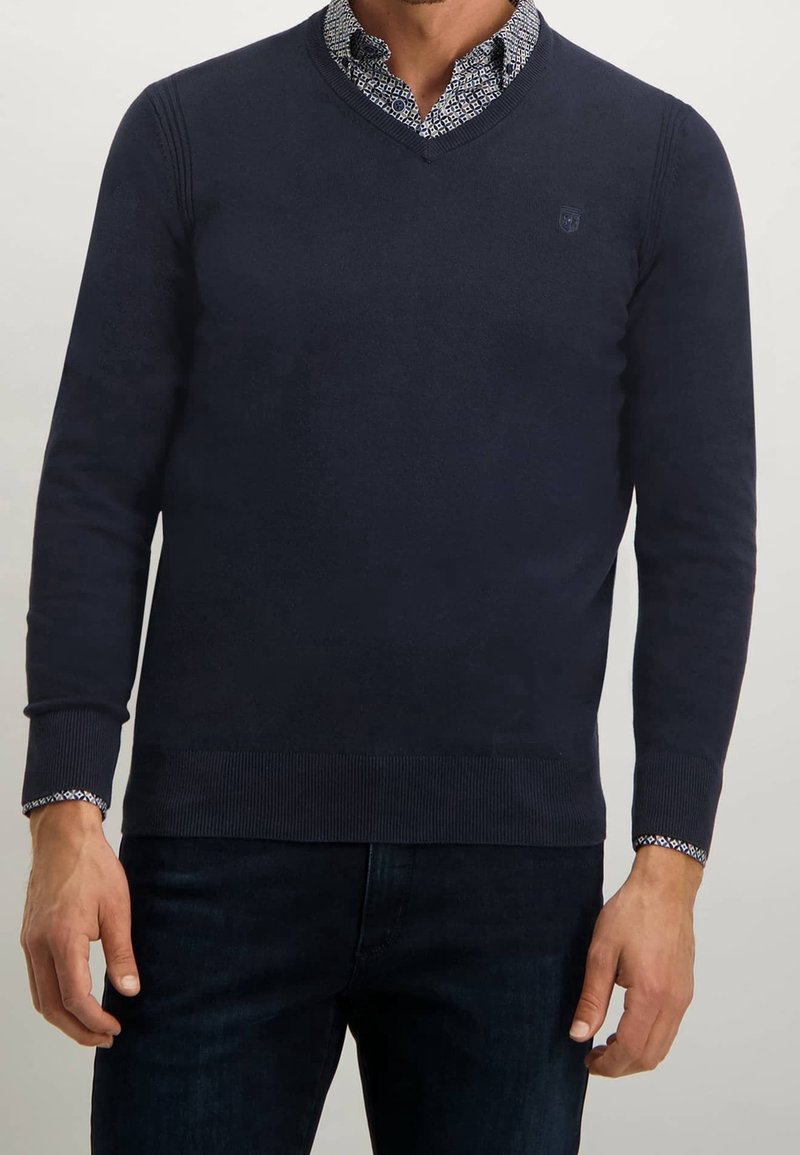 Marinblå V-ringad tröja i mjukt material, med ribbade ärmslut och fåll, samt en mönstrad skjortkrage synlig under.