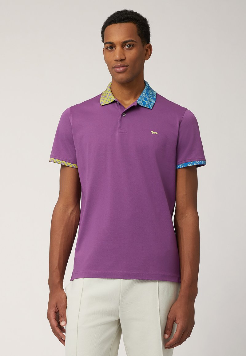 Lila polo-shirt med mönstrad krage i blått och gult, med korta ärmar och en liten logotyp på vänster sida.