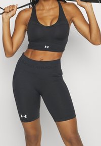 Crop top de sport noir et shorts en matériau extensible. Présente une texture lisse, un dos nageur et des accents de logo contrastants.