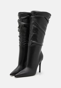 Schwarze, hochhackige Stiefel mit spitzen Zehen, aus glattem Leder gefertigt. Das Design verfügt über gerafftes Material an der Oberseite für zusätzliche Textur.