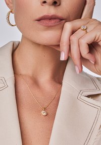 Złota naszyjnik z okrągłym wisiorkiem z centralnym kamieniem, w zestawie ze złotymi kolczykami w kształcie kółek ozdobionymi małymi kryształkami.