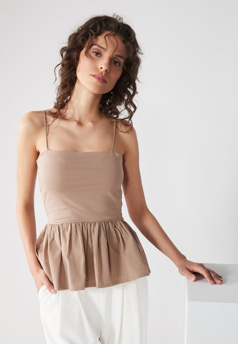 Lys brun peplum topp med tynne stropper, med en tettsittende bodice og flagrende midje. Glatt tekstur; enkel design uten mønstre.