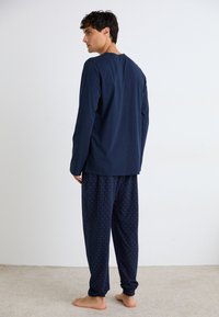 Marineblauwe longsleeve top met ronde hals, gecombineerd met gestreepte pyjamabroek met kleine rode en blauwe verticale lijnen. Katoenen stof.