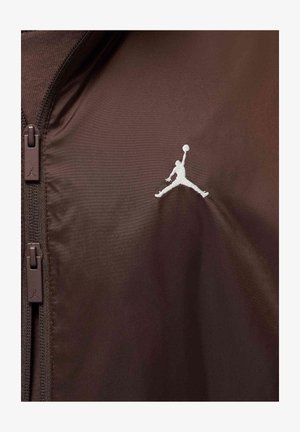 Brązowa kurtka z tkaniny z wysokim kołnierzem i zapinana na zamek, z białym logo Jumpman na piersi i brązowymi zamkami błyskawicznymi.