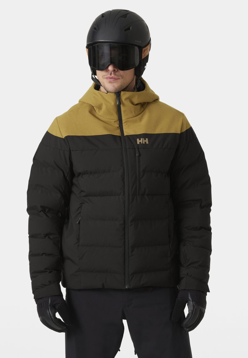 Schwarze und goldene isolierte Jacke mit einem Reißverschluss vorne, Kapuze und gestepptem Design. Das Logo befindet sich auf der Brust.