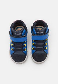 Blå och marinblå högskor med gula öglor, mocka tåhättor och ett kardborrefäste. Har en vadderad krage och gummisula.