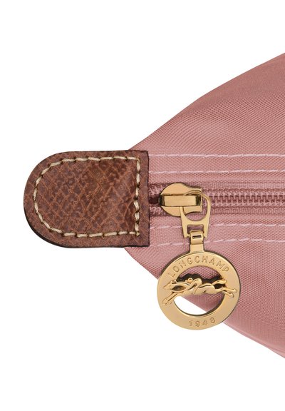 Pink nylon pouch with brown leather zipper pull, gold hardware featuring a round charm embossed with "LONGCHAMP 1948." Textured detail on leather.