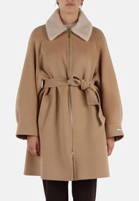 Cappotto in lana color sabbia con zip frontale, colletto in pelliccia, cintura in vita e tasche laterali. Presenta maniche larghe e una silhouette dritta.
