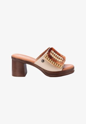 Mules beige de punta abierta con parte superior transparente, acentos de cinta dorada y un tacón grueso marrón. La suela está texturizada para proporcionar agarre.