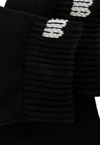 Schwarzer, gerippter Strickstoff mit teilweise weißem Text, der am Rand gestickt ist, wahrscheinlich Teil eines Kleidungsstücks oder Accessoires.