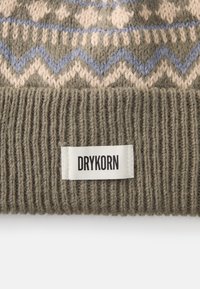 Gorro de malha em verde-azeitona com padrão em zigue-zague em creme e azul claro; a bainha canelada dobrada apresenta uma etiqueta de tecido branca com "DRYKORN."