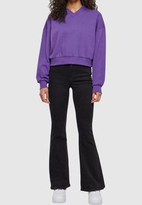 Felpa viola a collo a V con maniche lunghe e larghe, abbinata a jeans neri a vita alta a zampa e sneakers bianche. Tessuto dalla consistenza liscia.