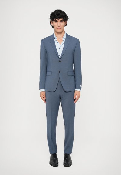Traje ajustado de color azul claro hecho de tela texturizada; blazer de un solo pecho, pantalones de corte plano, acompañado de una camisa de color azul claro. Zapatos negros.