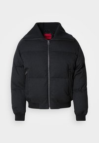 Veste matelassée noire à fermeture éclair avec col haut et large, poignets et ourlet côtelés, deux poches latérales zippées, et étiquette intérieure rouge.