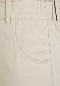 Närbild av ljusbruna tygbyxor med en synlig ficka och en bältesögla på midjebandet.