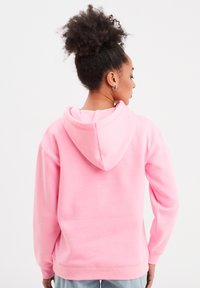 Felpa con cappuccio rosa chiaro dal taglio comodo, con polsini e orlo a costine. Il tessuto è morbido e ha una superficie liscia. Il cappuccio è regolabile.