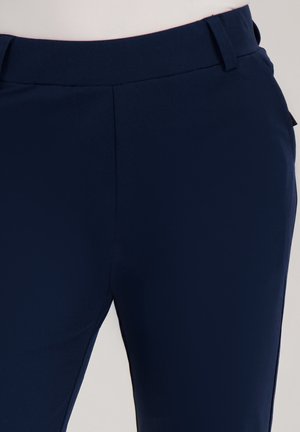 Op maat gemaakte marineblauwe broek met riemlussen, een gladde voorkant en een getailleerde taille op een neutrale achtergrond.