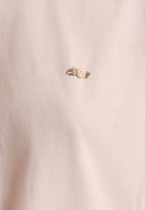 Jasnoróżowa tkanina z małym haftowanym różowym kwiatem z dwoma zielonymi liśćmi, umieszczonym na środku powierzchni.