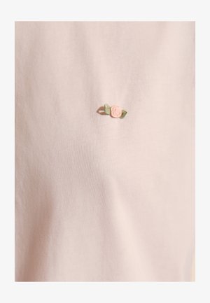 Jasnoróżowa tkanina z małym haftowanym różowym kwiatem z dwoma zielonymi liśćmi, umieszczonym na środku powierzchni.