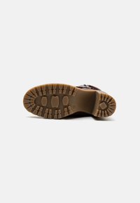 Brown leather boot sole with deep treads, featuring a rubber outsole and thick cushioning. Notable grooves for traction and durability.