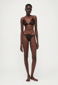 Conjunto de soutien e tanga em renda preta com padrões florais, alças ajustáveis e bordas delicadas sobre a pele nua.