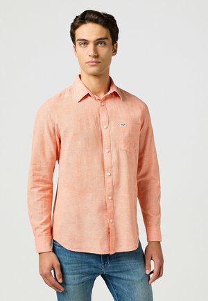 Light orange long-sleeve shirt with a button-up front, single chest pocket, and subtle texture. Paired with blue jeans.
