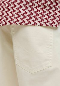 Gros plan d'une poche de pantalon en denim blanc sous un tissu texturé à motif pied-de-poule rouge et blanc.