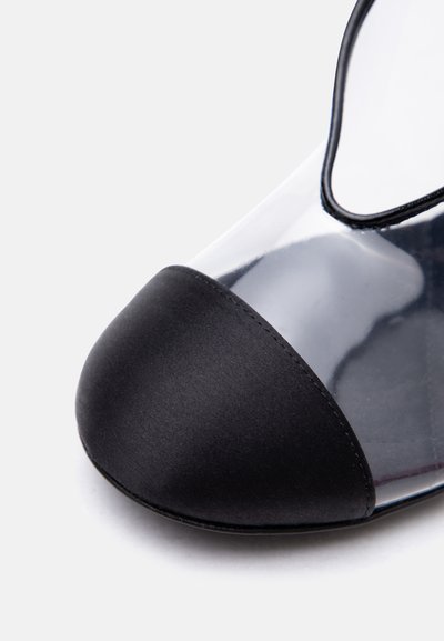 Prim-plan al unei capete negre pe o încălțăminte plată transparentă, cu margine neagră și finisaj neted.