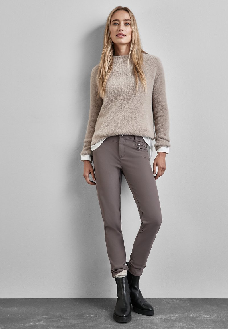 Beige, fluffy sweater over een witte blouse, gecombineerd met verstelbare grijze broek en zwarte enkellaarsjes. Bondig ontwerp met eenvoudige lijnen.