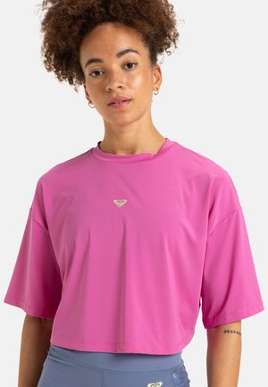 Pink cropped athletic t-shirt with short sleeves, featuring a round neckline and a small gold logo accent on the chest. Soft texture.