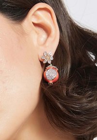Orecchini color oro con design floreale e strass sopra un pendente rotondo corallo che scintilla con gemme trasparenti.