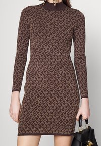 Robe en tricot marron à manches longues, dotée d'un motif géométrique dans une teinte plus claire. Col montant et design ajusté.