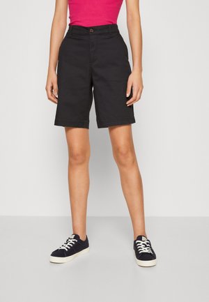 Shorts en coton noir avec une coupe droite, dotés d'une fermeture à bouton, de poches avant et d'un ourlet roulé. Associés à des baskets bleu marine.