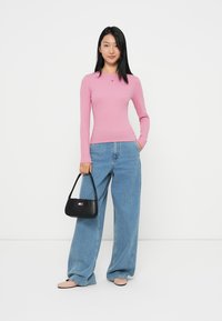Pink long-sleeve top paired with wide-leg blue jeans. A black handbag features a colored logo. Smooth fabric and relaxed fit.