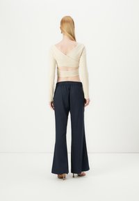 Maglietta beige a maniche lunghe con design incrociato sul retro abbinata a pantaloni wide-leg blu scuro, caratterizzati da una vestibilità comoda e un elastico in vita.