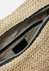 Borsa in tessuto beige con superficie texturizzata, zip nera e interno liscio con una tasca con zip aggiuntiva.