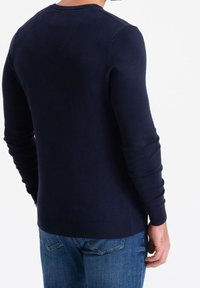 Tummansininen neulepaita, jossa on pitkät hihat, taitetut hihansuut, pyöreä pääntie ja sileä pinta. Näkyvä selkädesign ja tiukka malli.