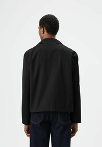 Zwarte jas met een klassieke kraag, een ontspannen pasvorm en lange mouwen, gemaakt van lichtgewicht stof. Details zijn onder andere een gladde textuur en een minimalistisch ontwerp.