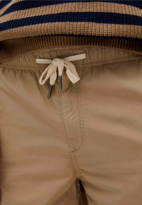 Khaki shorts med elastisk talje og beige snøre. De har en glat stoftekstur og et simpelt design uden synlige mønstre.