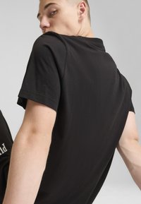 Czarny bawełniany t-shirt z krótkim rękawem i okrągłym dekoltem. Charakteryzuje się luźnym krojem, gładką fakturą oraz minimalnymi detalami na plecach.