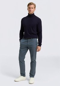 Laivastonsininen korkeakauluksinen neule yhdistettynä vaaleanharmaisiin housuihin ja valkoisiin tennareihin; sileät pintarakenteet, istuva muotoilu ja moderni ilme.