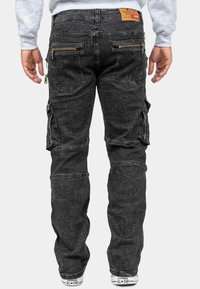 Jeans cargo neri con molte tasche con zip, una finitura testurizzata e un taglio dritto. Abbinati a sneakers bianche e una felpa grigia.