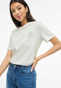 Jasnoszara koszulka z krótkim rękawem, z kwiatowym konturem i napisem "wild soul" w różowym haftie na lewej piersi.