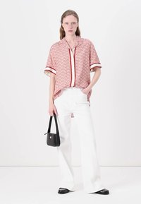 Rood geometrisch patroon kortemouwen shirt met een knoopkraag, gecombineerd met witte wijde jeans en een kleine zwarte handtas. Zwarte platte schoenen.