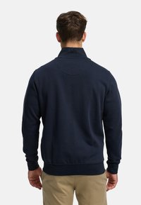 Mörkblå sweatshirt med hög krage, ribbade ärmslut och fåll. Har en slät textur och detalj med söm bak.