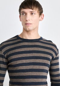 Pull rayé aux couleurs bleu marine et beige, en tissu texturé, avec un col rond, des manches longues et une coupe près du corps.