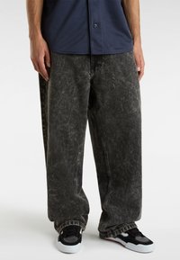 Vaqueros anchos de pierna ancha, de lavado ácido negro con textura descolorida, combinados con zapatillas negras y blancas. Presentan un ajuste holgado y puños rematados.