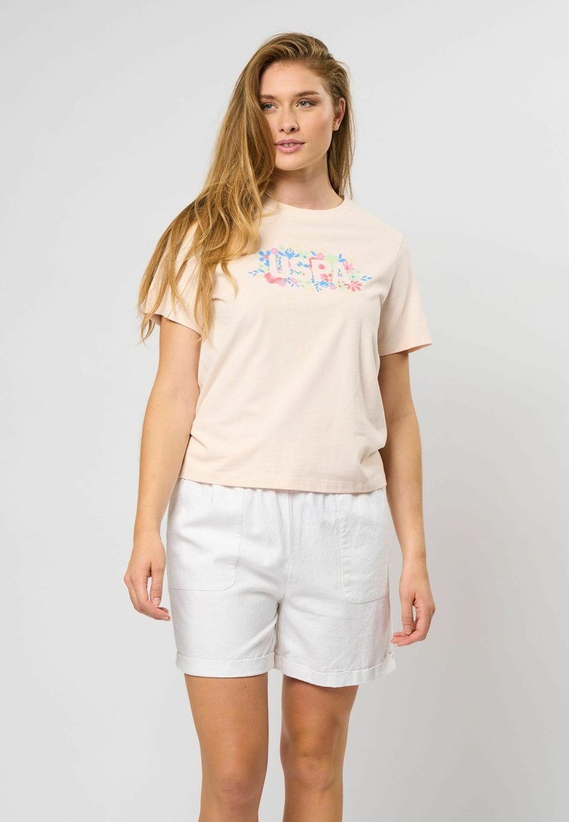 Lys rosa bomull t-skjorte med et fargerikt "USPA" blomsterdesign. Kombinert med hvite shorts, som viser en avslappet passform og en uformell stil.