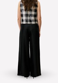 Zwarte broek met brede pijpen gecombineerd met een zwart-wit geruit mouwloos topje met een gestructureerd geweven ontwerp.