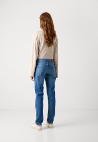 Beige langermet topp, blå denimjeans med middels høy midje, teksturert stoff, og lyse sko med gummisåle.